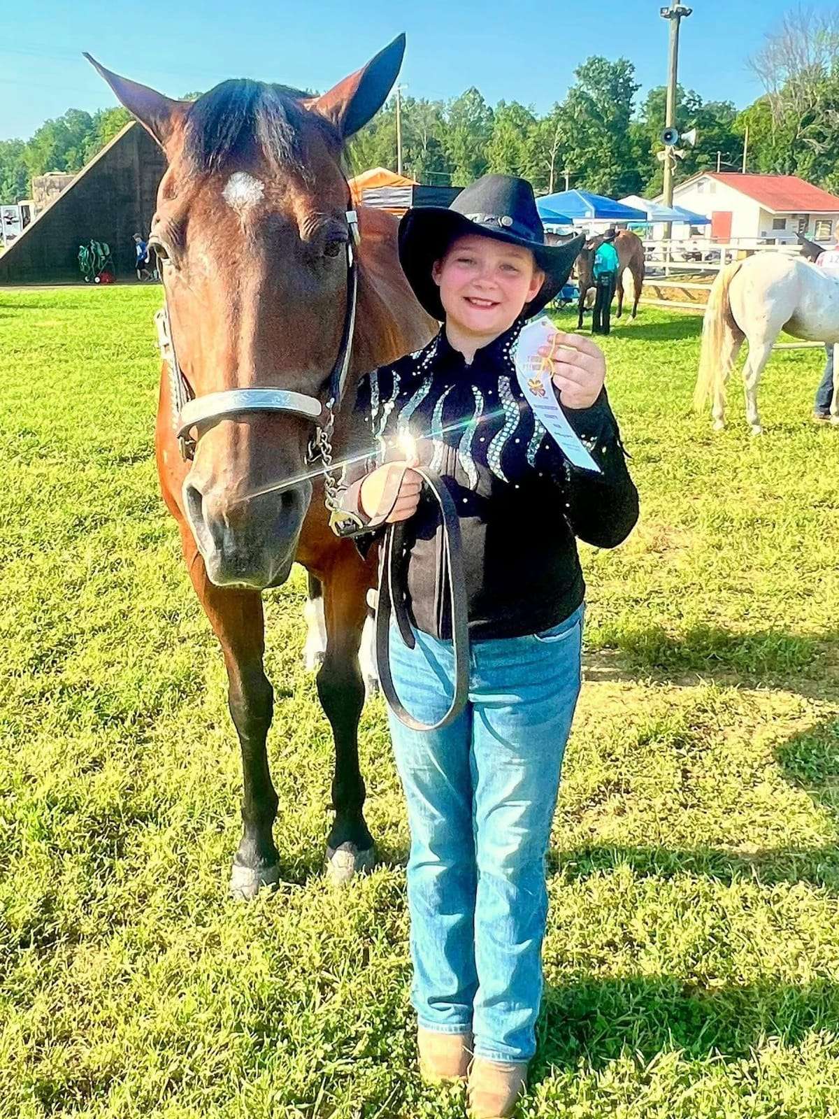4-H rider in western show attire holding an award beside her horse