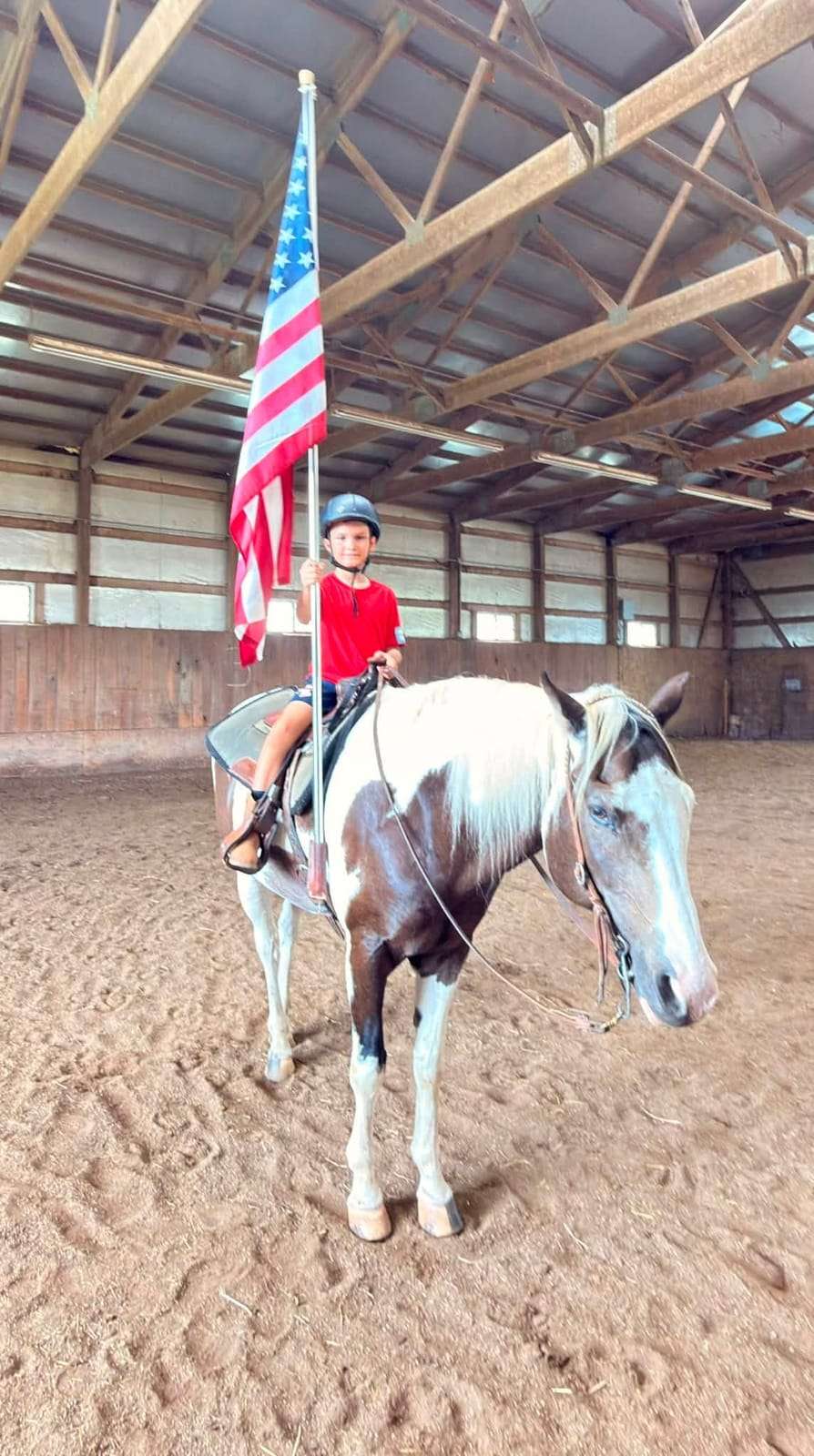 Camper carrying an American flag on a grey horse in the arena