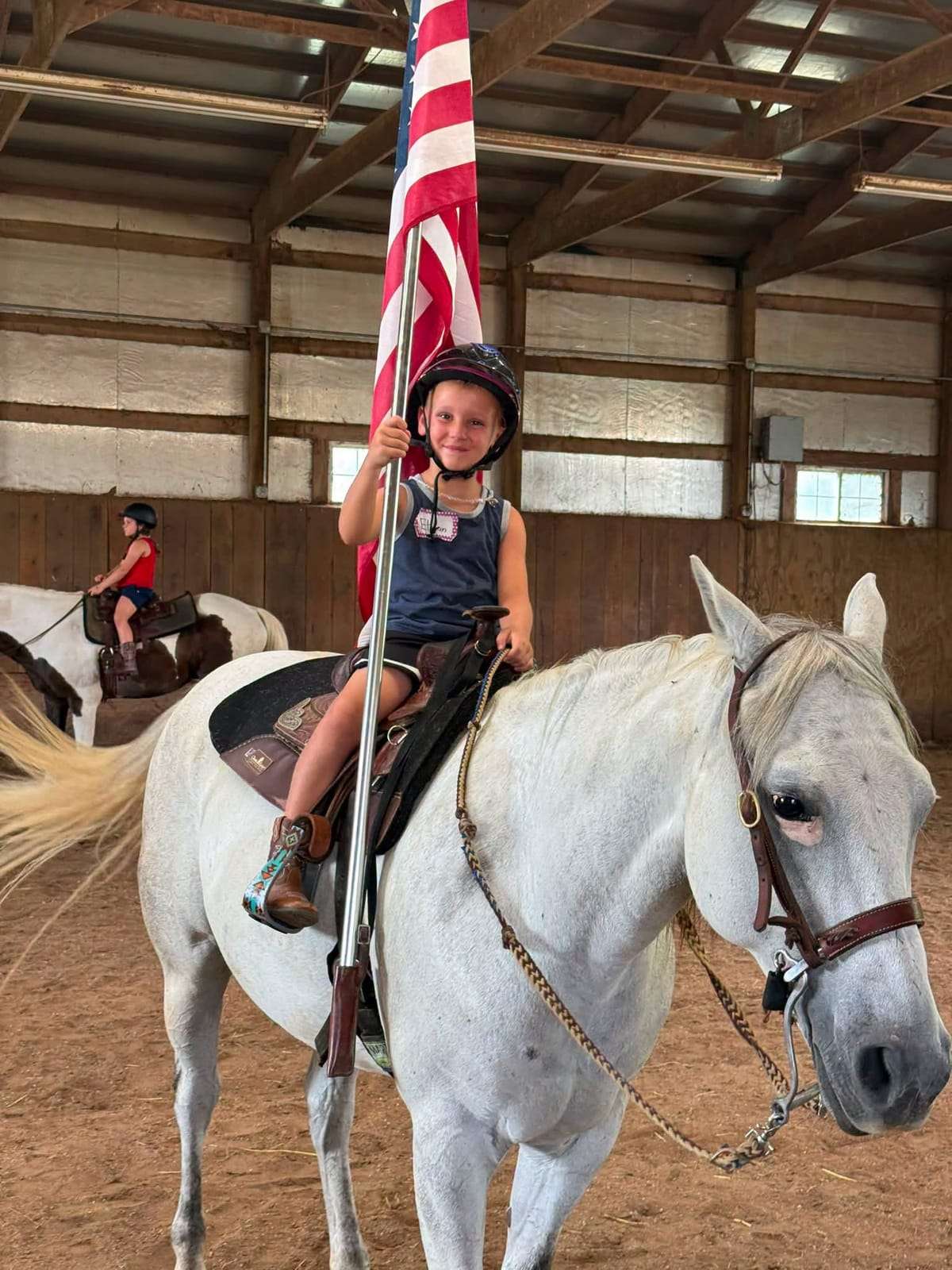 Camper carrying the American flag on a grey horse