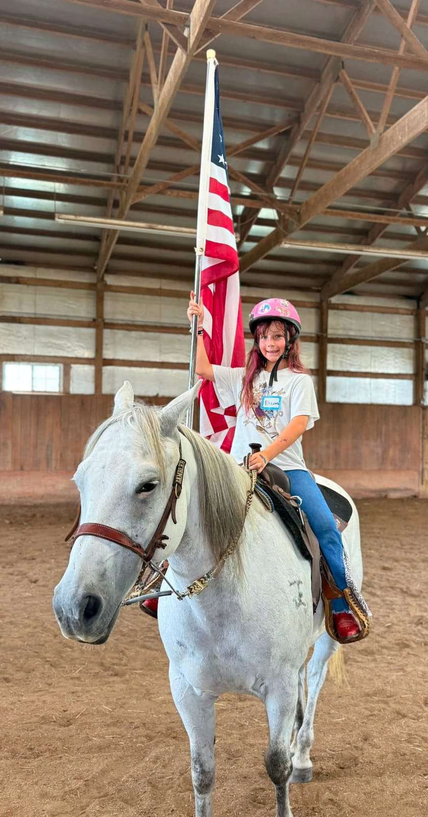 Camper carrying an American flag on a grey horse