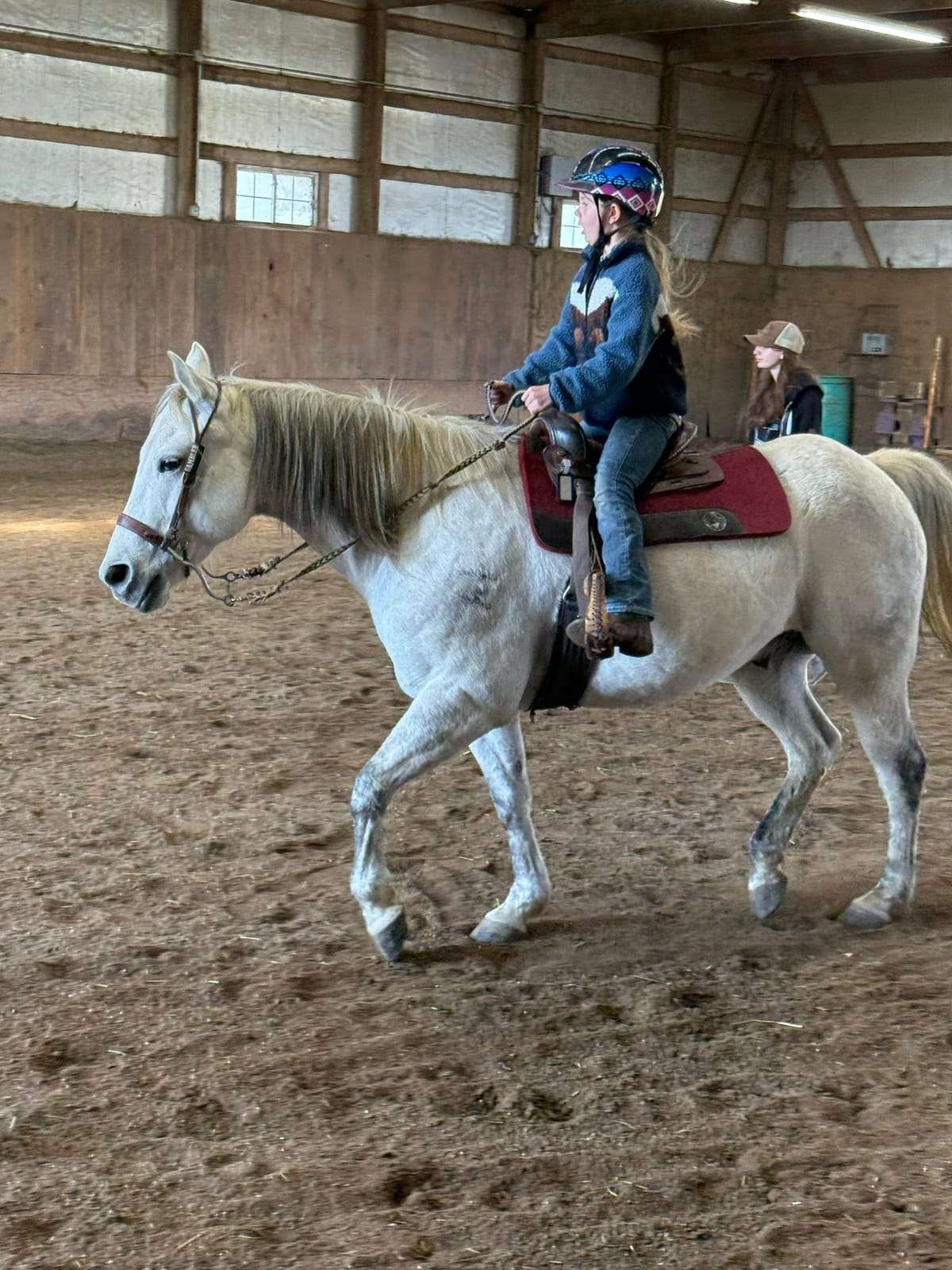Camper riding a grey horse in the indoor arena