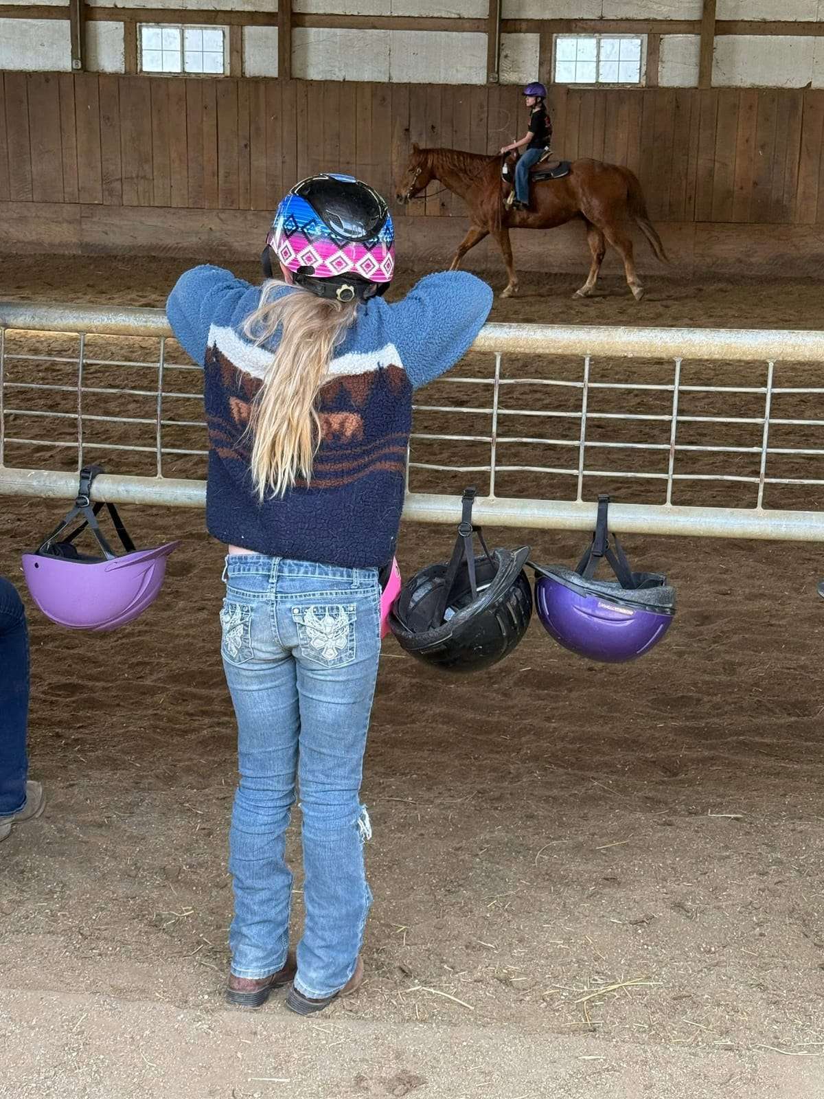 Camper watching a riding lesson with helmets on the rail