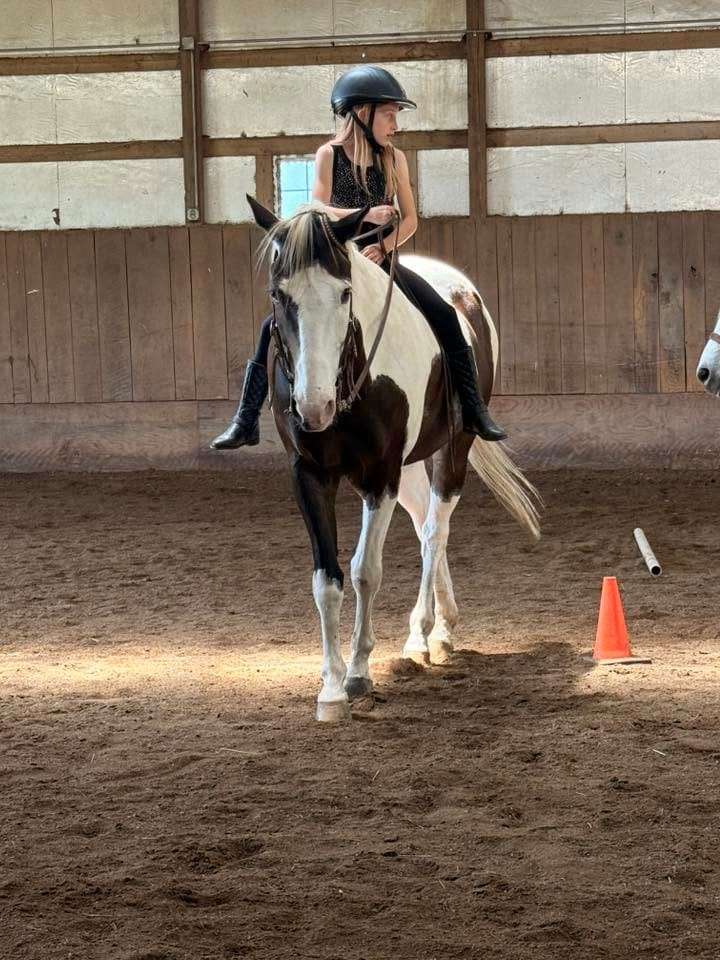 A camper riding a paint horse in the arena