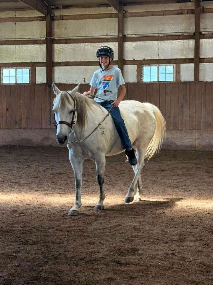 A camper riding a grey horse during summer camp
