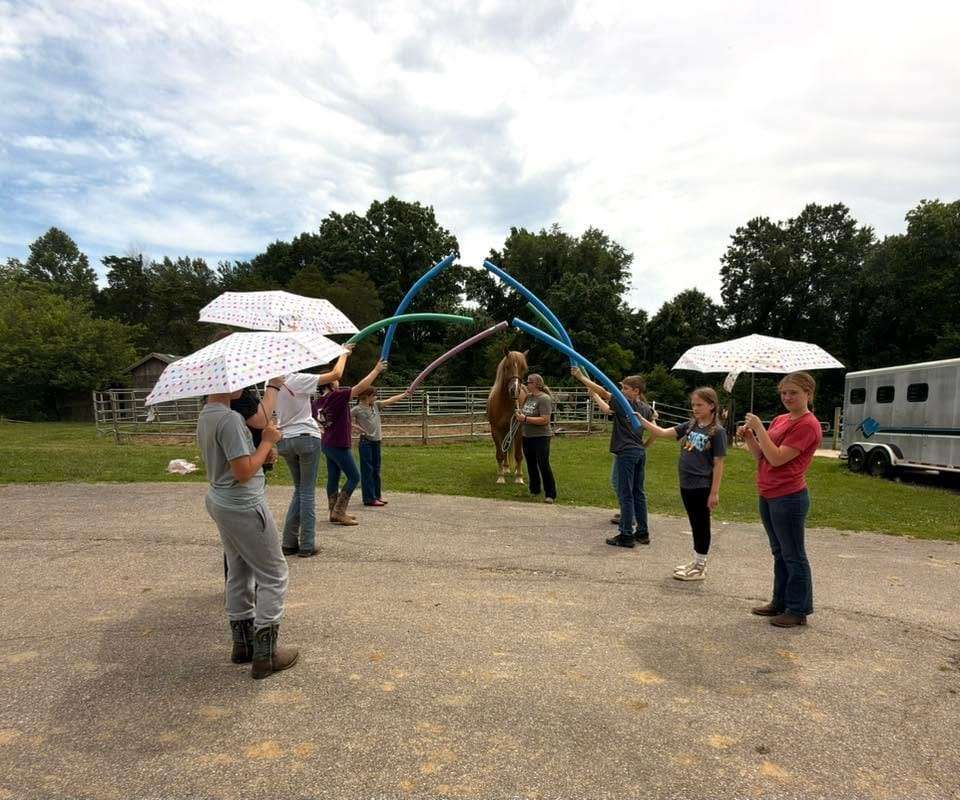 Campers forming a line for a teamwork activity with pool noodles and umbrellas
