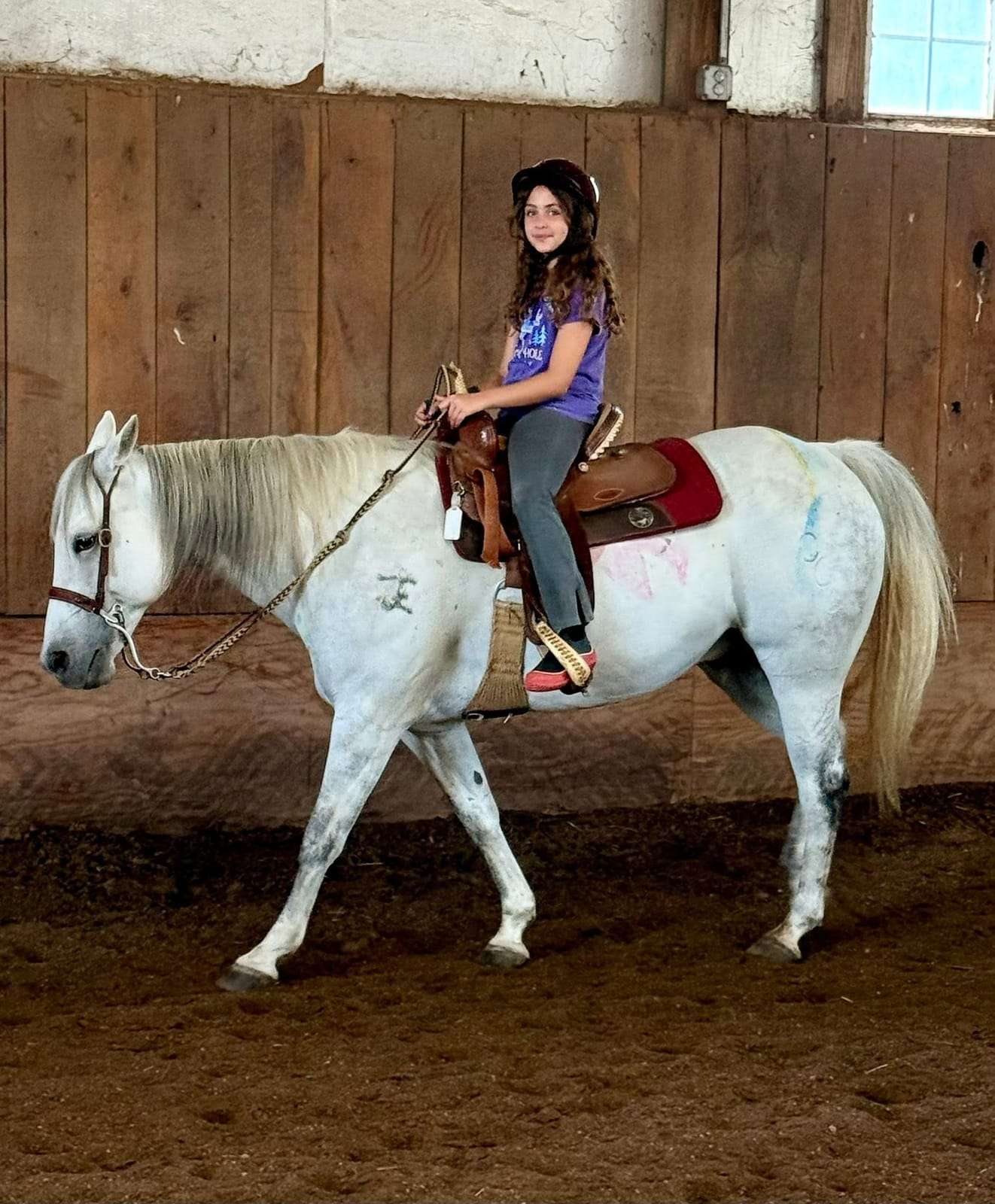 Camper riding a grey horse in the arena
